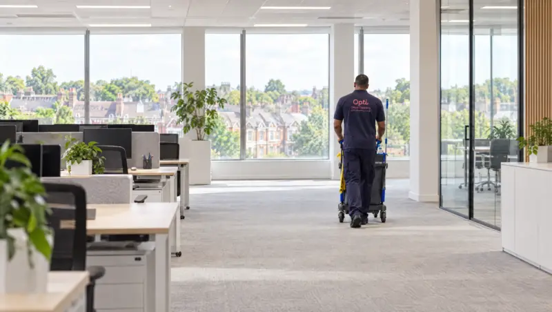 An Opti Clean operative with a cleaning trolley in a bright open-plan office