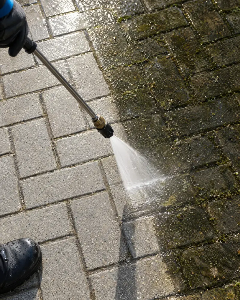 Close-up of a commercial pressure washer lifting grime from block paving
